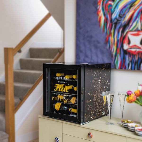 Husky Prosecco Drinks Cooler with black exterior and gold confetti design, holding bottles inside on a cabinet.