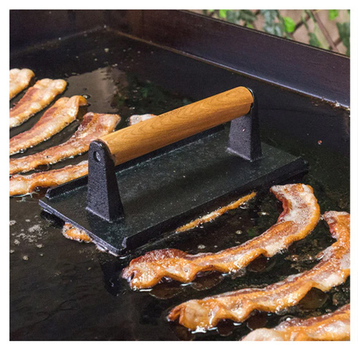 Blackstone Breakfast Kit bacon press with wooden handle on griddle cooking bacon strips