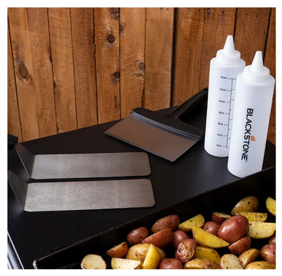 Blackstone 5230EU Griddle Essentials Toolkit with two scrapers and two squeeze bottles on griddle top with cooked potatoes
