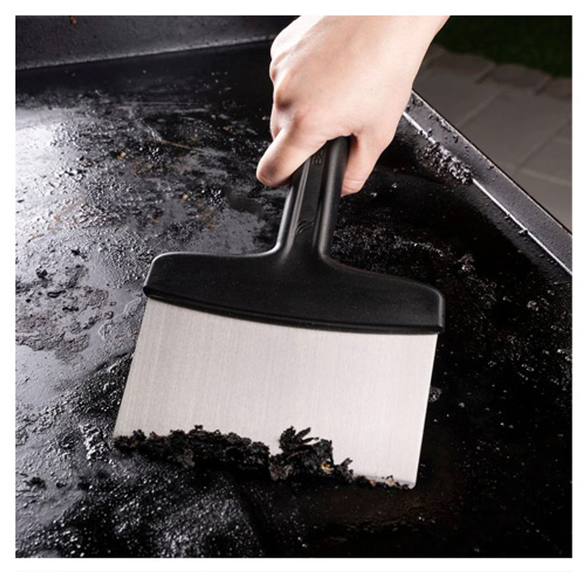 Hand using Blackstone 5230EU griddle scraper to remove burnt residue from griddle surface