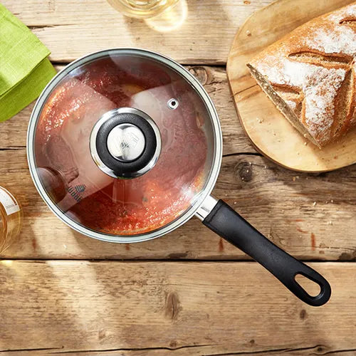 Judge Vista 16cm saucepan with glass lid, black handle, filled with tomato sauce on wooden table next to bread.