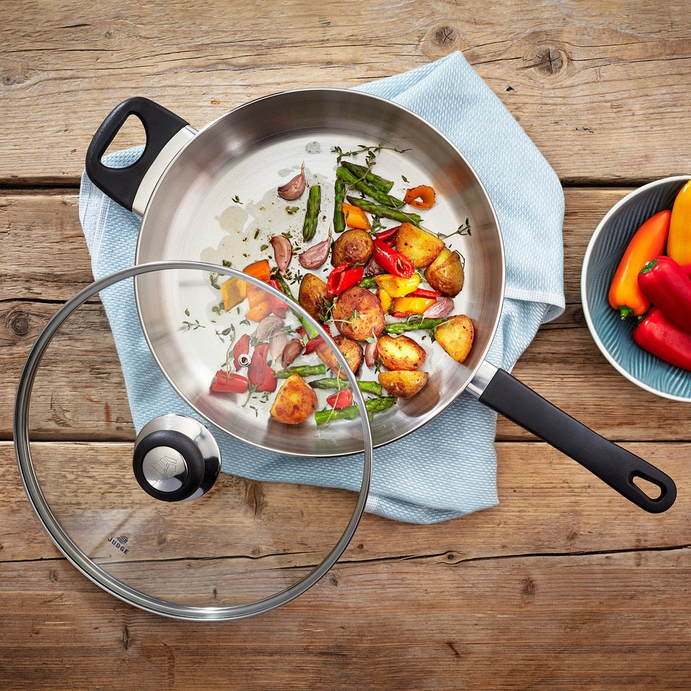 Judge Vista 28cm saute pan with glass lid, containing cooked vegetables on a wooden surface.