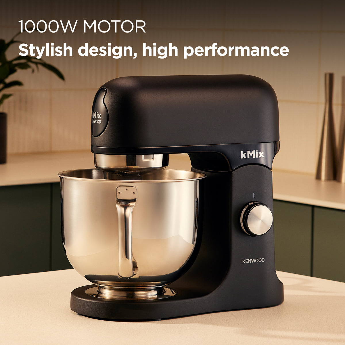 Kenwood kMix black stand mixer with stainless steel bowl on a kitchen counter in soft lighting