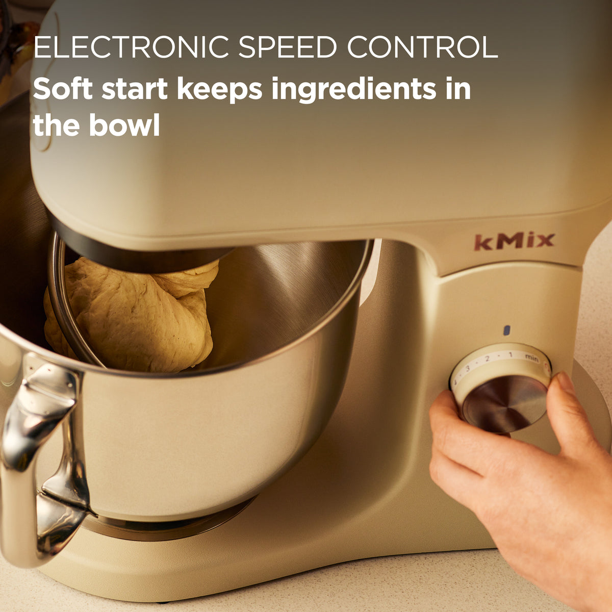 Kenwood kMix cream stand mixer with dough in bowl and hand adjusting speed control dial