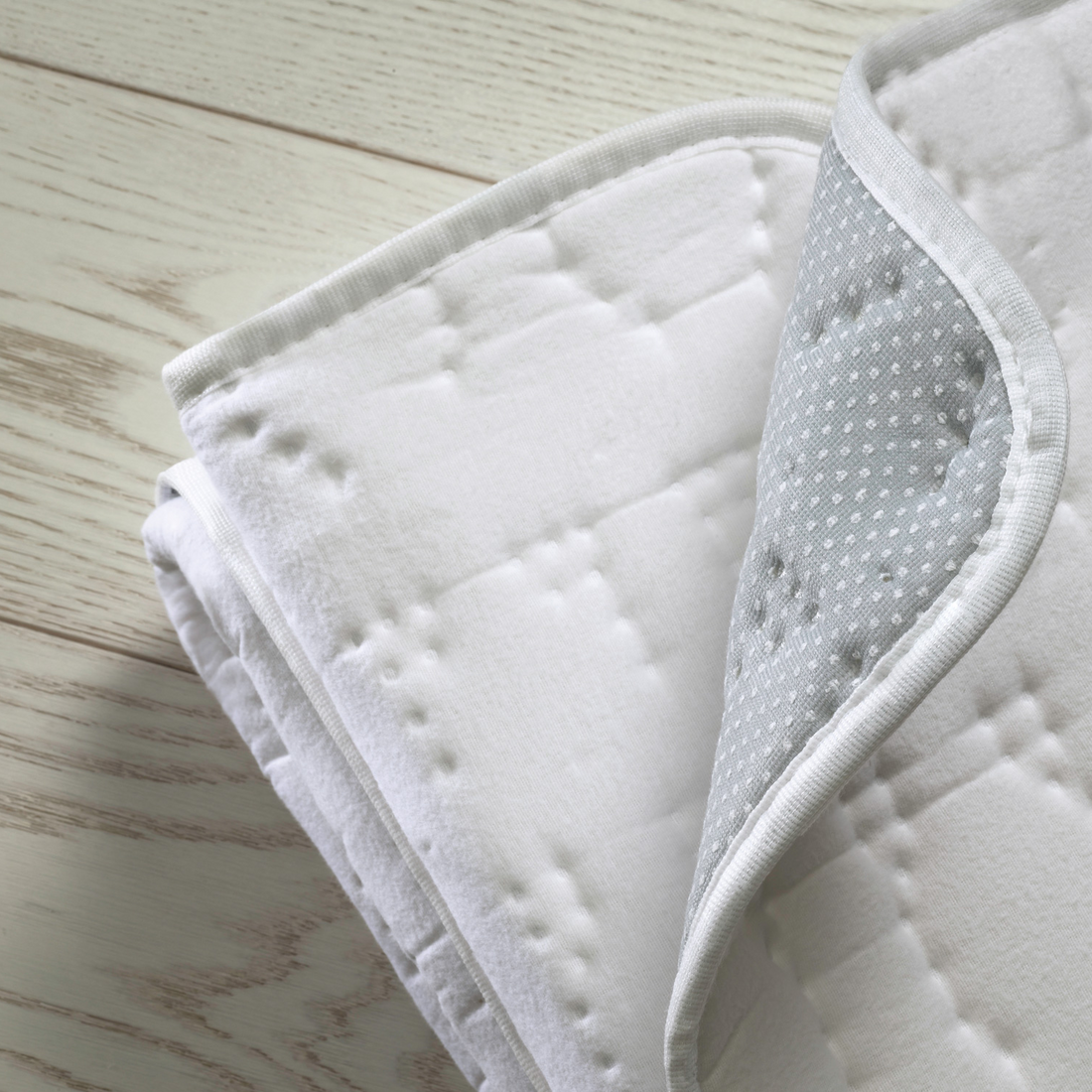 Folded Dreamland Cosy Dreamer Superior Cotton mattress protector showing white quilted top and grey dotted underside.