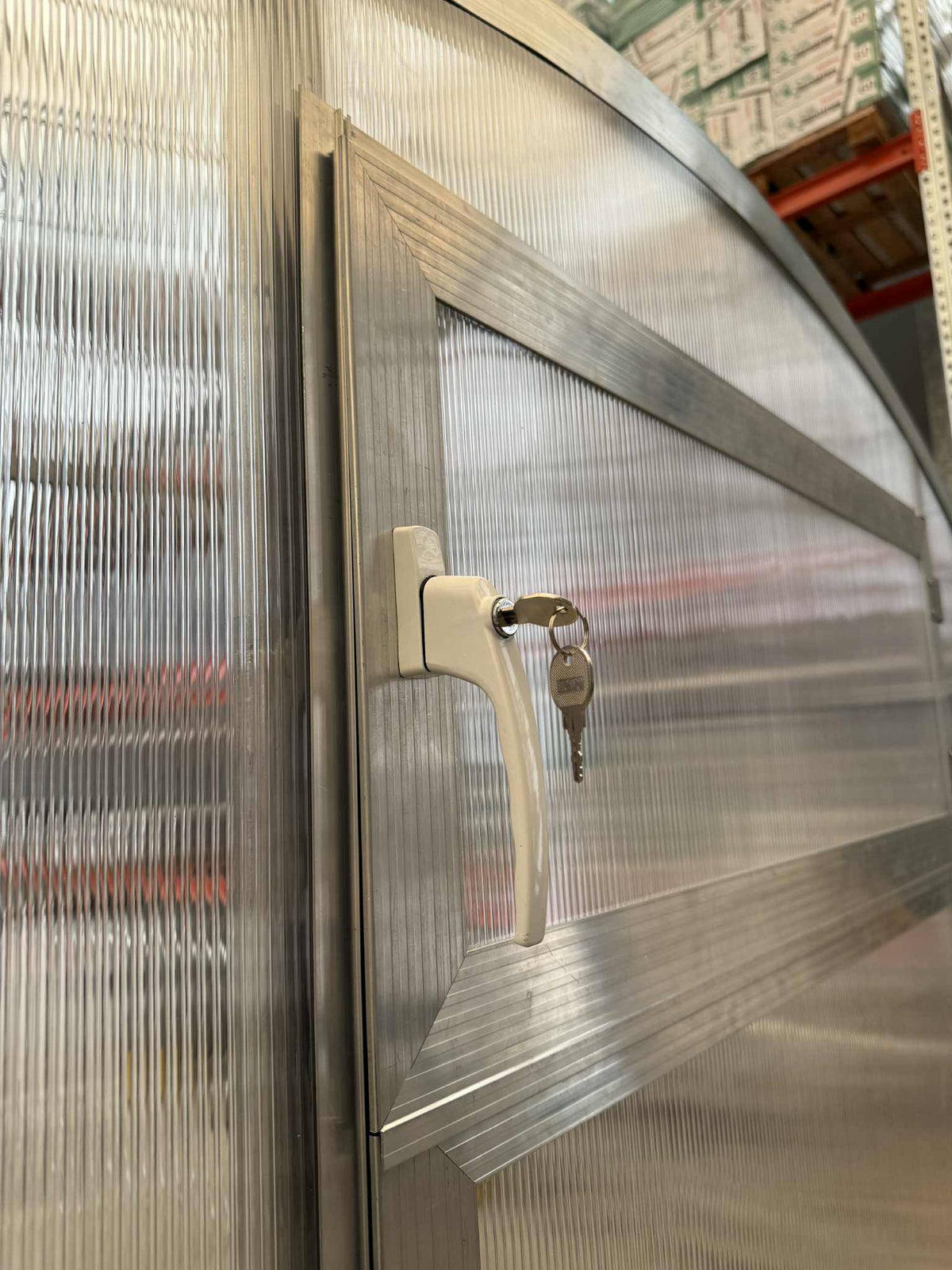 Close-up of Sigma Lux greenhouse door with white handle, key inserted, and 6mm polycarbonate panels