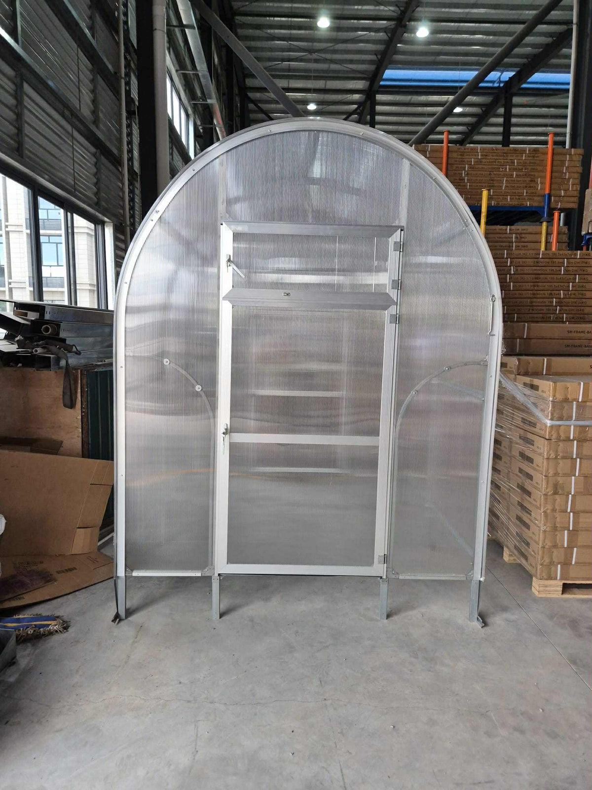 Front view of Sigma Lux 2m x 6m greenhouse with 6mm polycarbonate panels and a closed door inside a warehouse.
