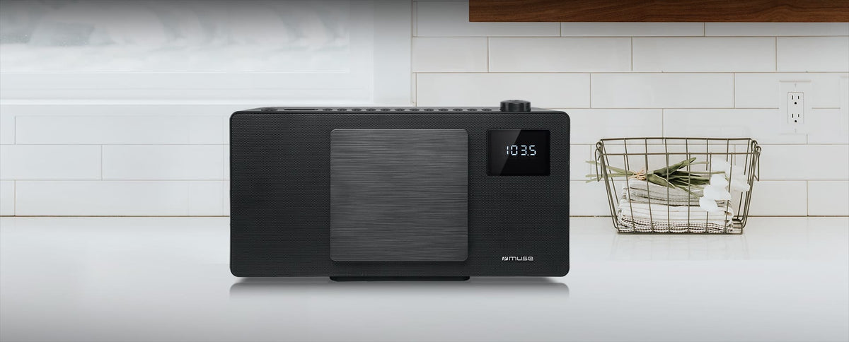 Black Muse CD BT Micro System with digital display showing FM radio frequency, placed on a white kitchen counter.