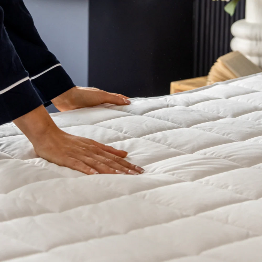 Hands pressing down on a quilted white Dreamland Snowed In organic cotton mattress protector on a bed.