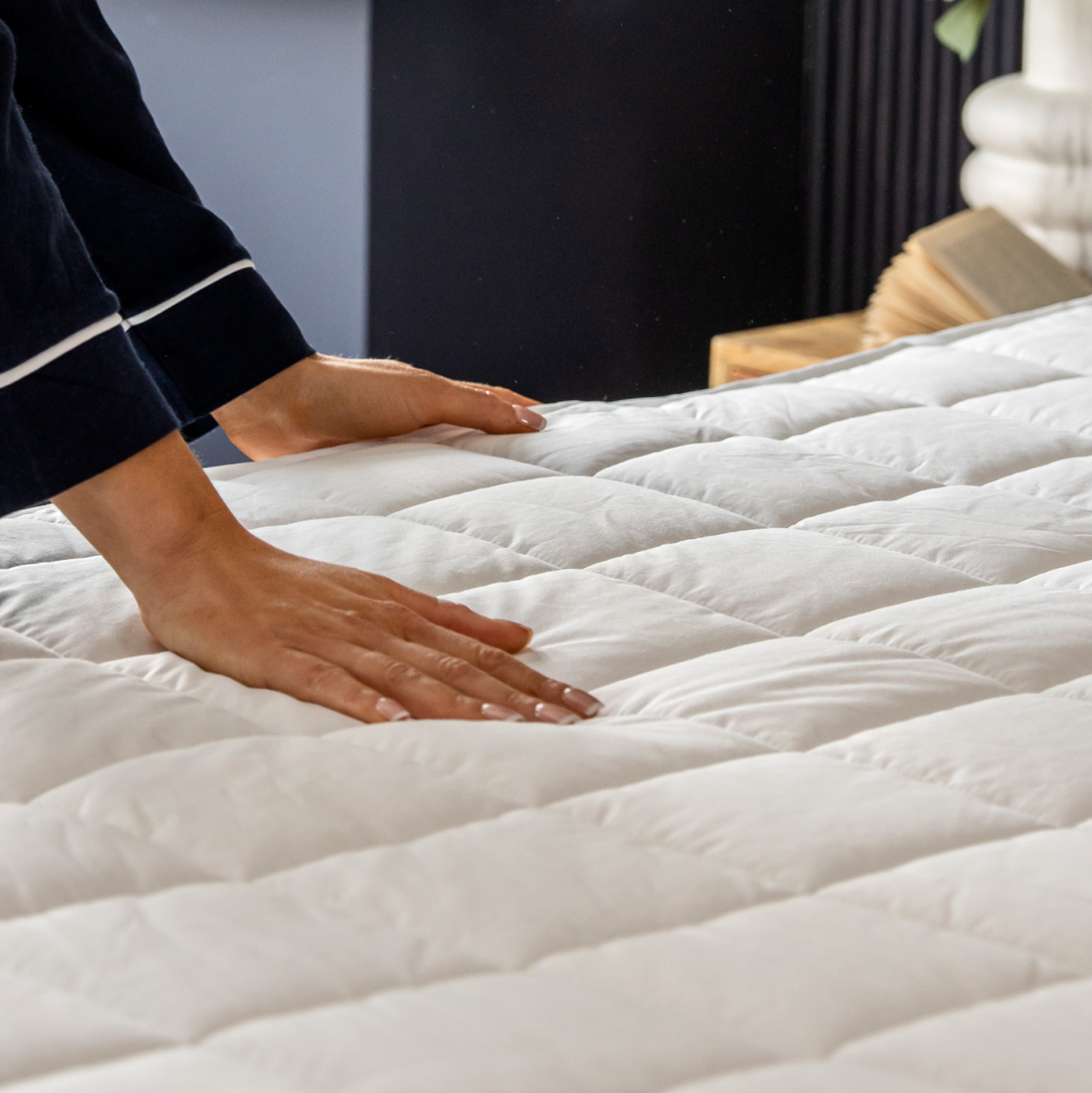 Hands smoothing a white quilted Dreamland Mattress Cover Electric Blanket on a bed.