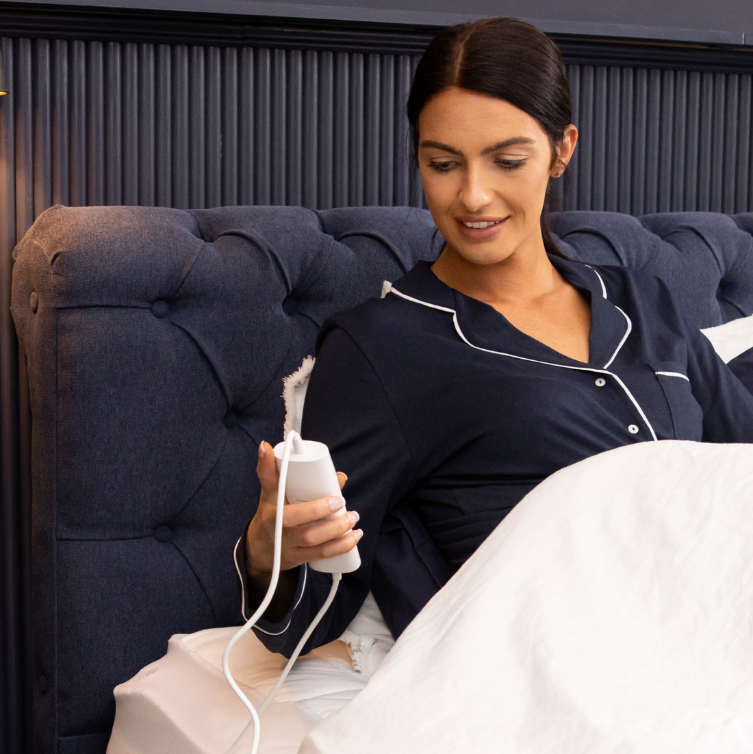 Woman in navy pajamas sitting on bed holding the controller of a Dreamland Mattress Cover Electric Blanket Single