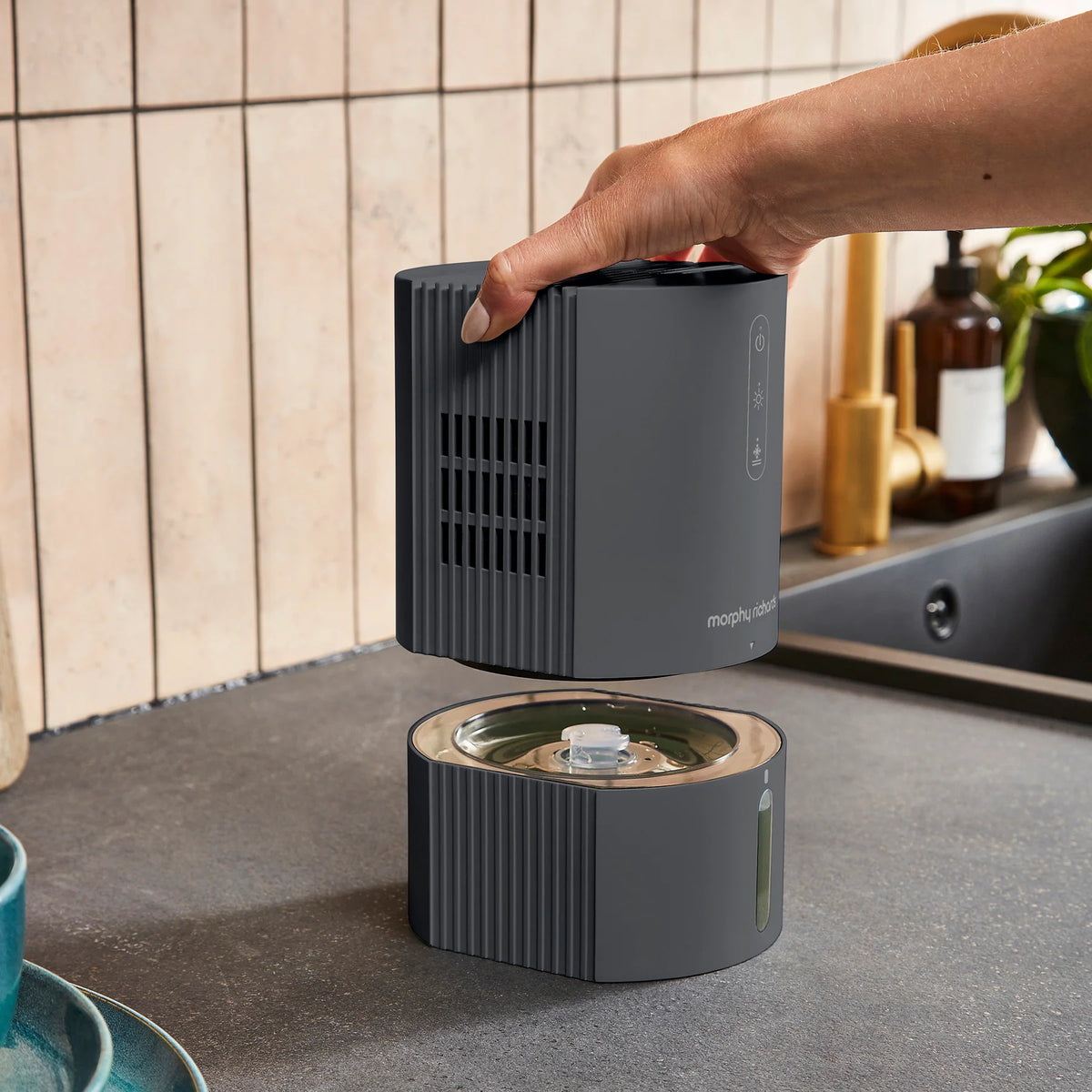 Hand lifting the top part of a black Morphy Richards Purefresh 0.9L dehumidifier on a kitchen counter.