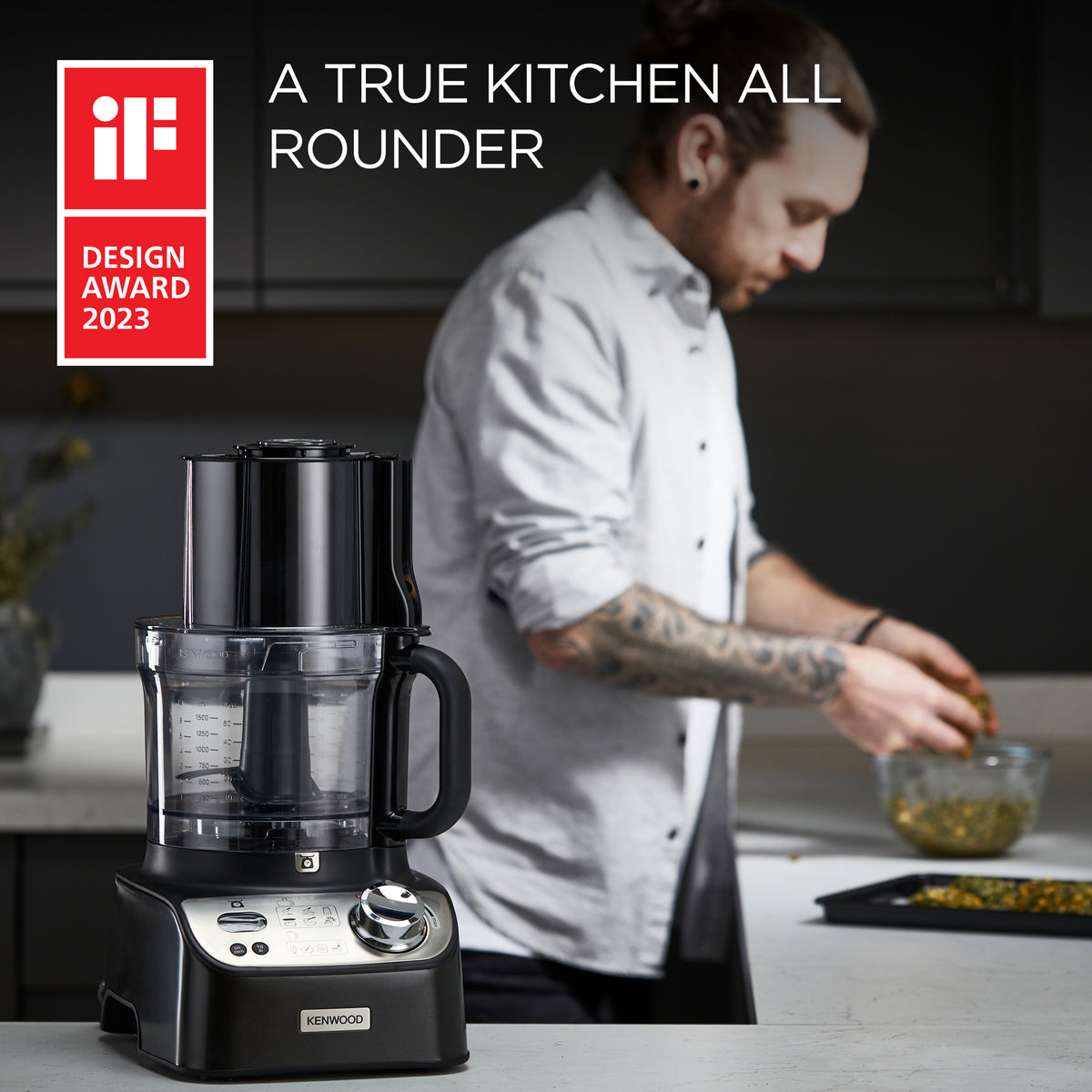 Kenwood MultiPro XL Weigh food processor with clear bowl and black base on kitchen counter, man cooking in background