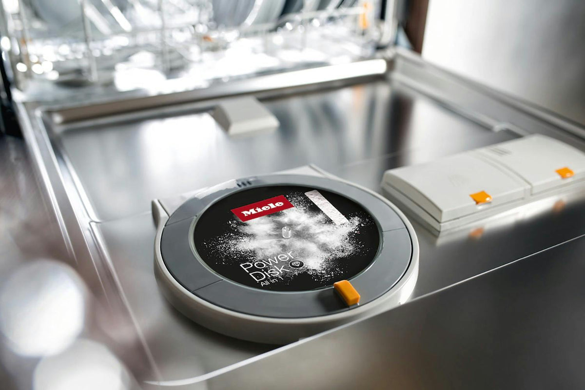 Miele PowerDisk dishwasher detergent placed inside a dishwasher detergent compartment with powder visible on top.