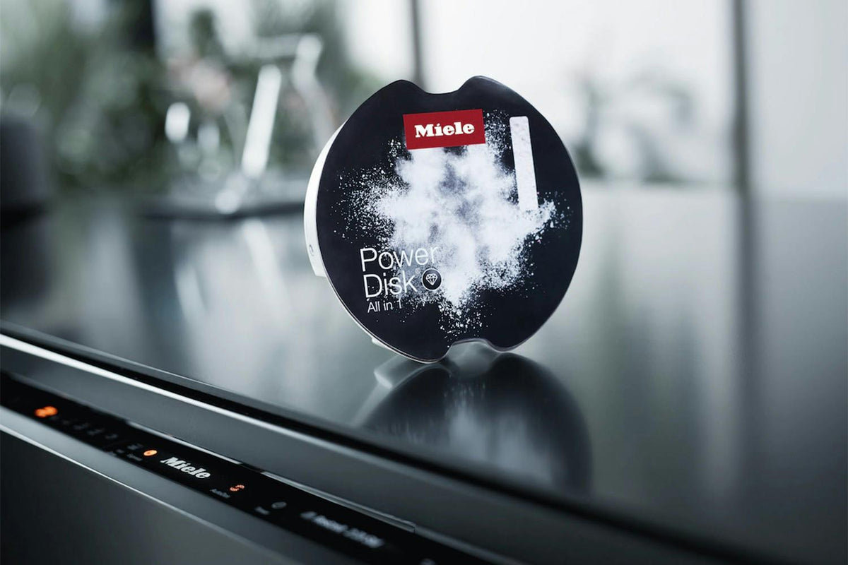 Miele PowerDisk single pod with powder burst design on a sleek black dishwasher surface.