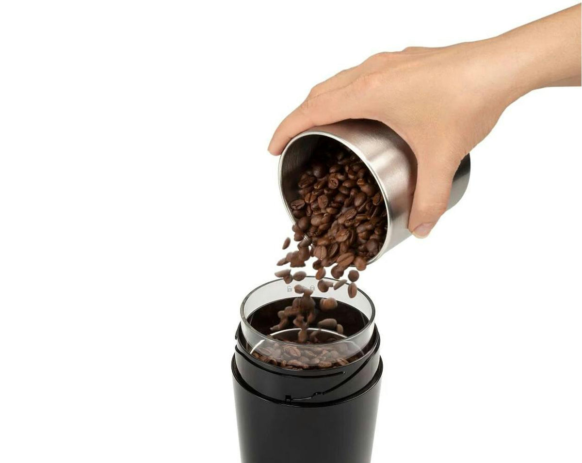 Hand pouring coffee beans into the open top of the Delonghi Electric Blade Coffee Grinder KG210.