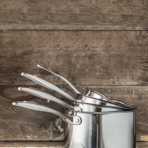 Stacked stainless steel saucepans with long handles against a rustic wooden background