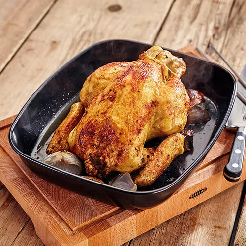 Stellar Bakeware non-stick roasting tray with a whole roasted chicken and onions on a wooden board