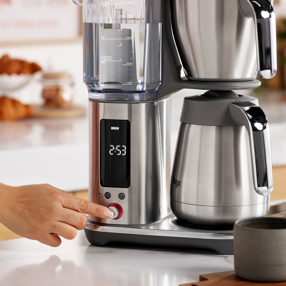 Hand pressing the start button on the Sage Precision Brewer Thermal Brushed Steel coffee maker with timer display.