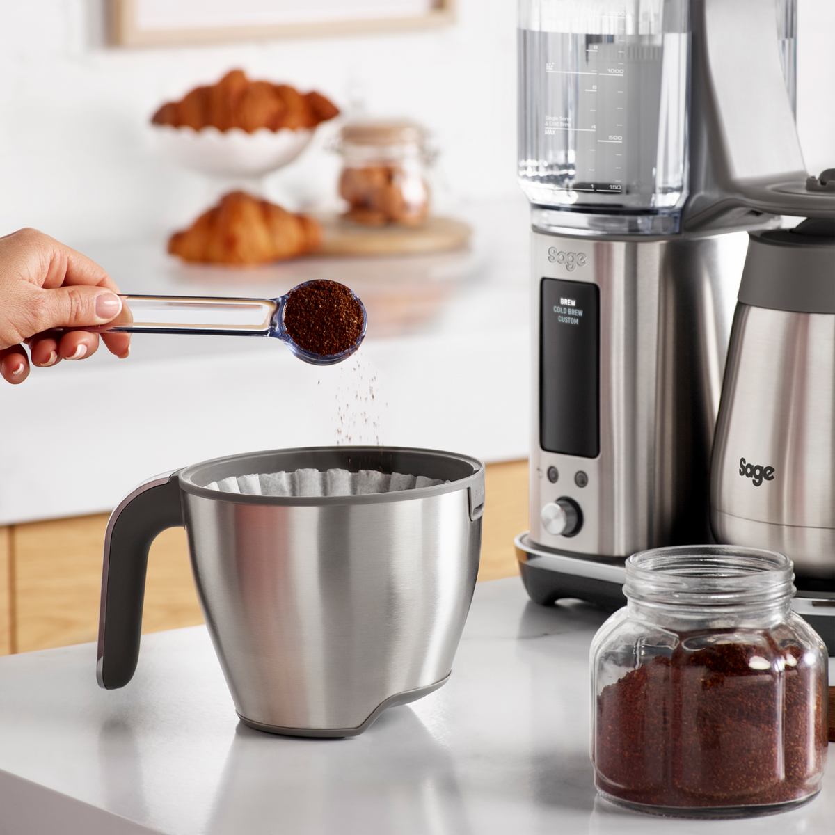 Sage Precision Brewer Thermal brushed steel filter basket with coffee grounds being added by hand.