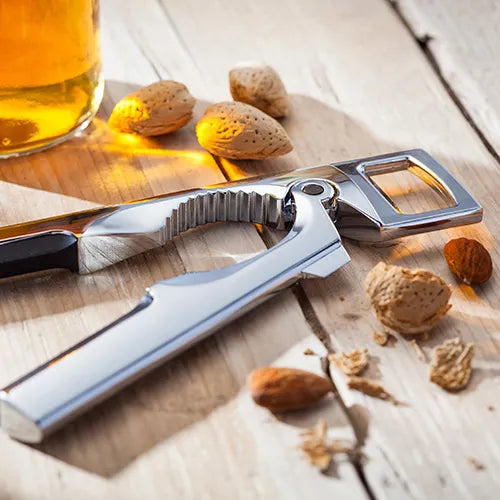 Stellar Nut Cracker and Bottle Opener in chrome finish on wooden surface with nuts and a glass of amber liquid nearby