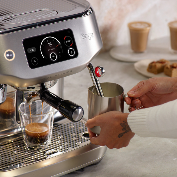 Sage Oracle Dual Boiler espresso machine steaming milk in a stainless steel jug with coffee brewing below.