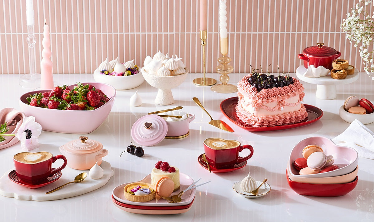 Stacked Le Creuset Heart Set 4 Plates in red, pink, and cream holding macarons on a white table.