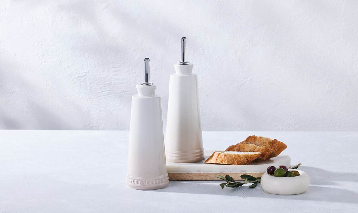 Le Creuset 330ml stoneware oil and vinegar set in meringue with bread slices and olives on a tray