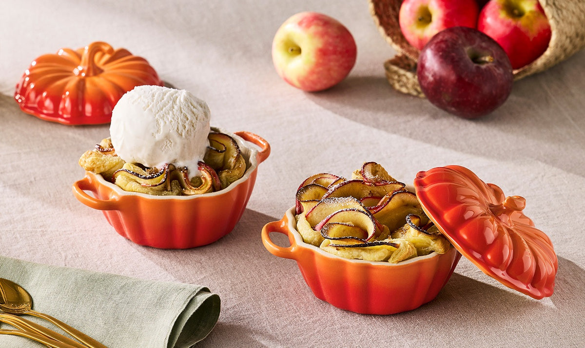 Two Le Creuset Halloween Pumpkin Casseroles in volcanic orange, one with ice cream on apple tart, one with lid off