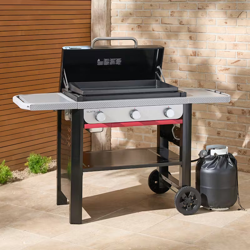 Weber Slate GP 71cm Premium Griddle with open lid, three control knobs, side shelves, and propane tank outdoors