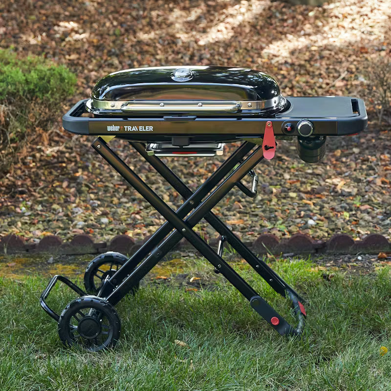 Weber Traveler portable gas barbecue with black lid and foldable stand on grass outdoors