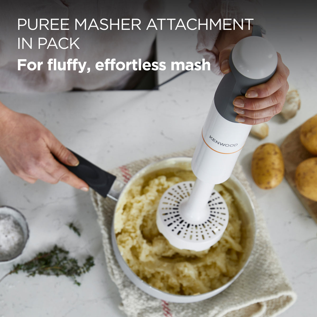 Hand holding Kenwood Triblade 850W masher attachment mashing potatoes in a bowl on a kitchen counter.