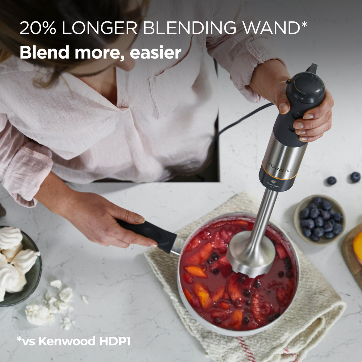 Person using Kenwood Triblade XL+ hand blender to blend fruit in a pot on a kitchen counter