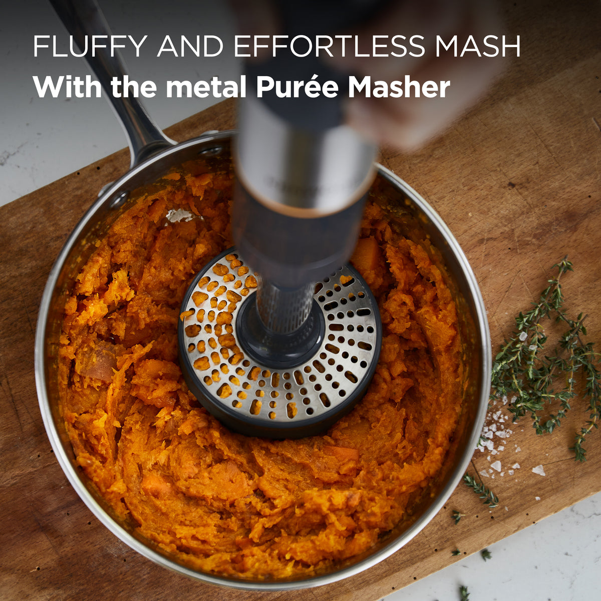 Kenwood Triblade XL+ metal purée masher mashing cooked orange vegetables in a pot on a wooden board