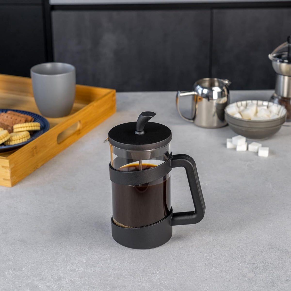 Style 8 Cup Cafetiere with black handle and lid filled with coffee on a kitchen counter with snacks and sugar cubes nearby