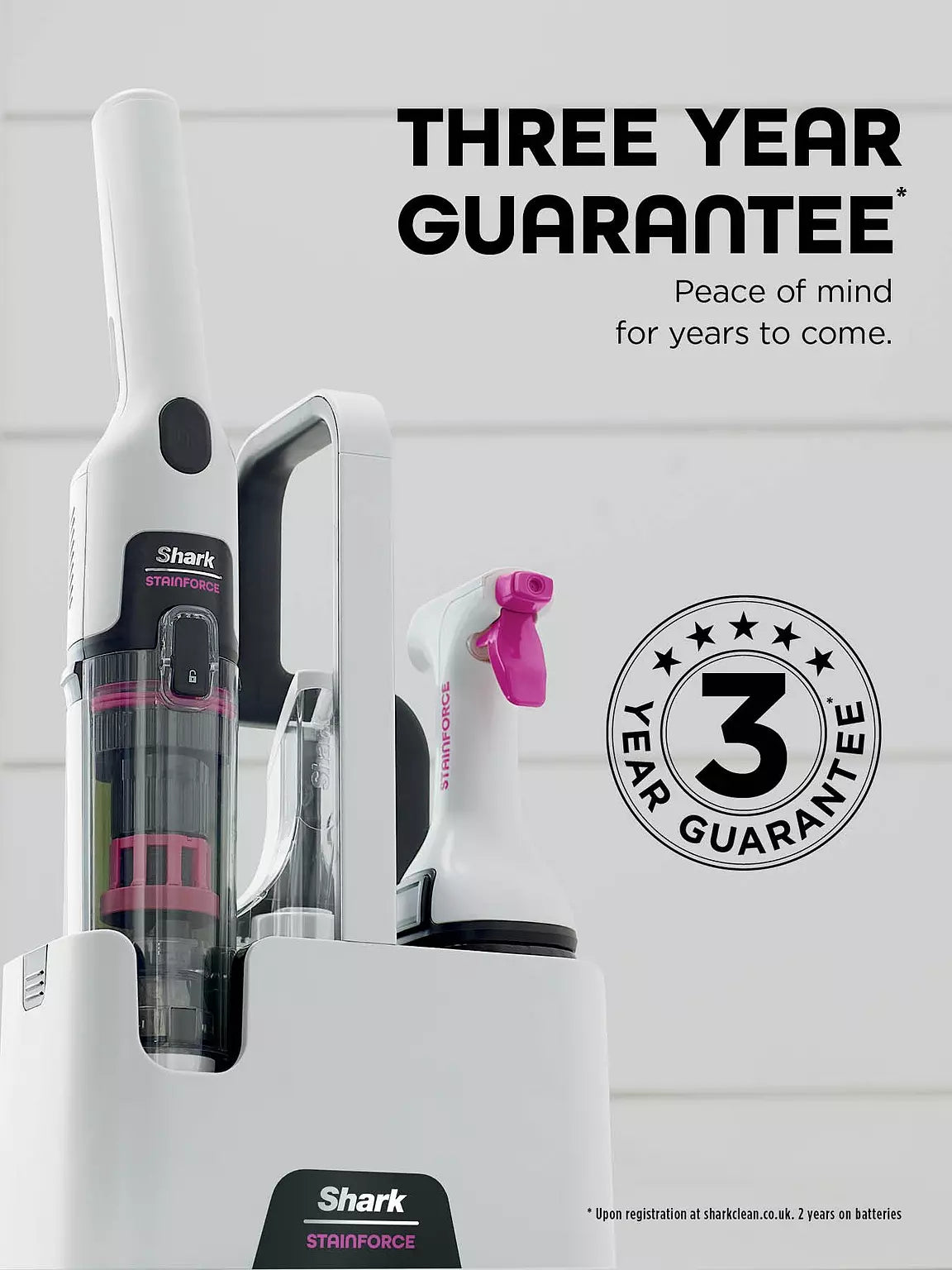 Shark Stainforce cordless spot cleaner in white with pink accents in its charging dock, showing a three-year guarantee.