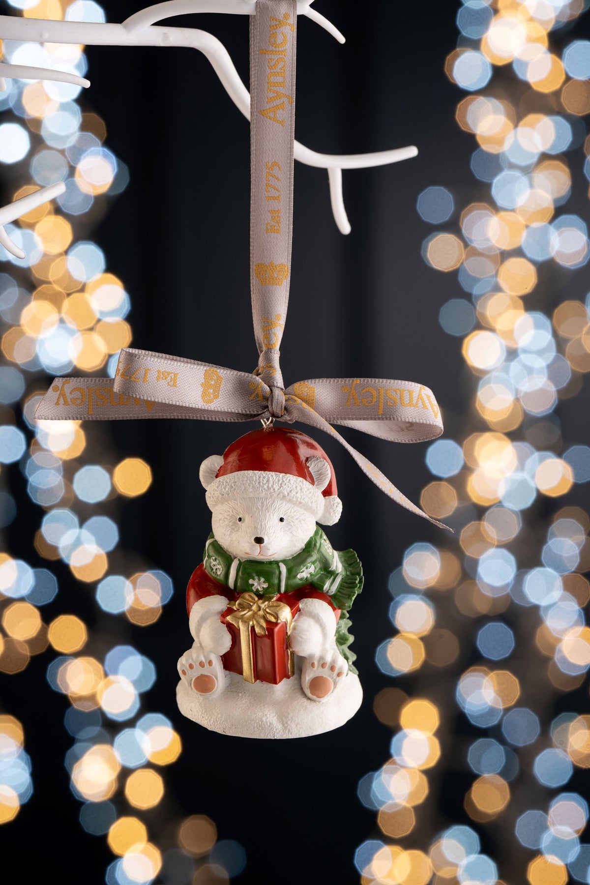 Aynsley polar bear ornament wearing a Santa hat and green scarf, holding a red gift with gold ribbon.