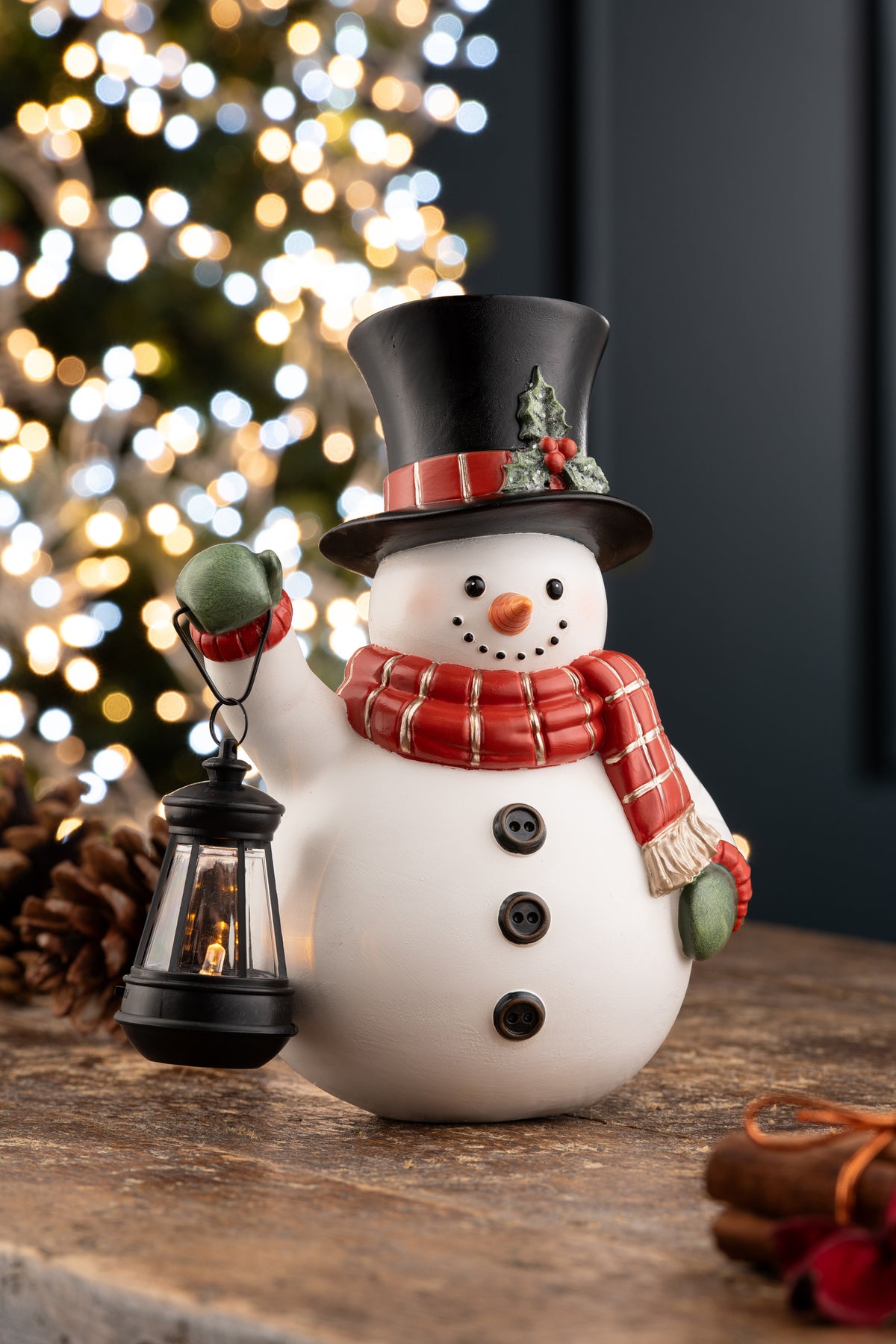 Aynsley LED snowman wearing a black top hat and red scarf, holding a lit lantern on a wooden surface.