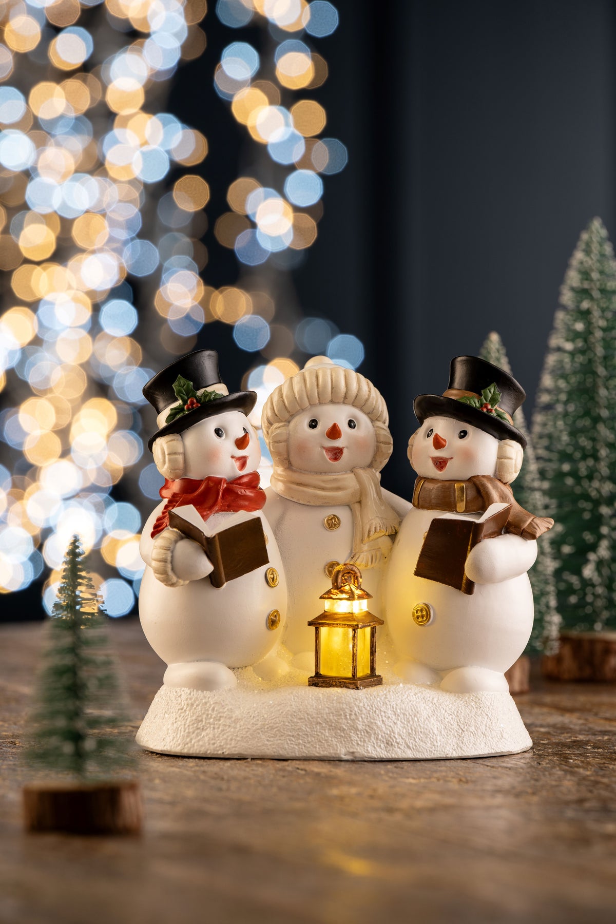 Trio of snowmen carol singers figurine with scarves, hats, songbooks, and a glowing lantern on snowy base