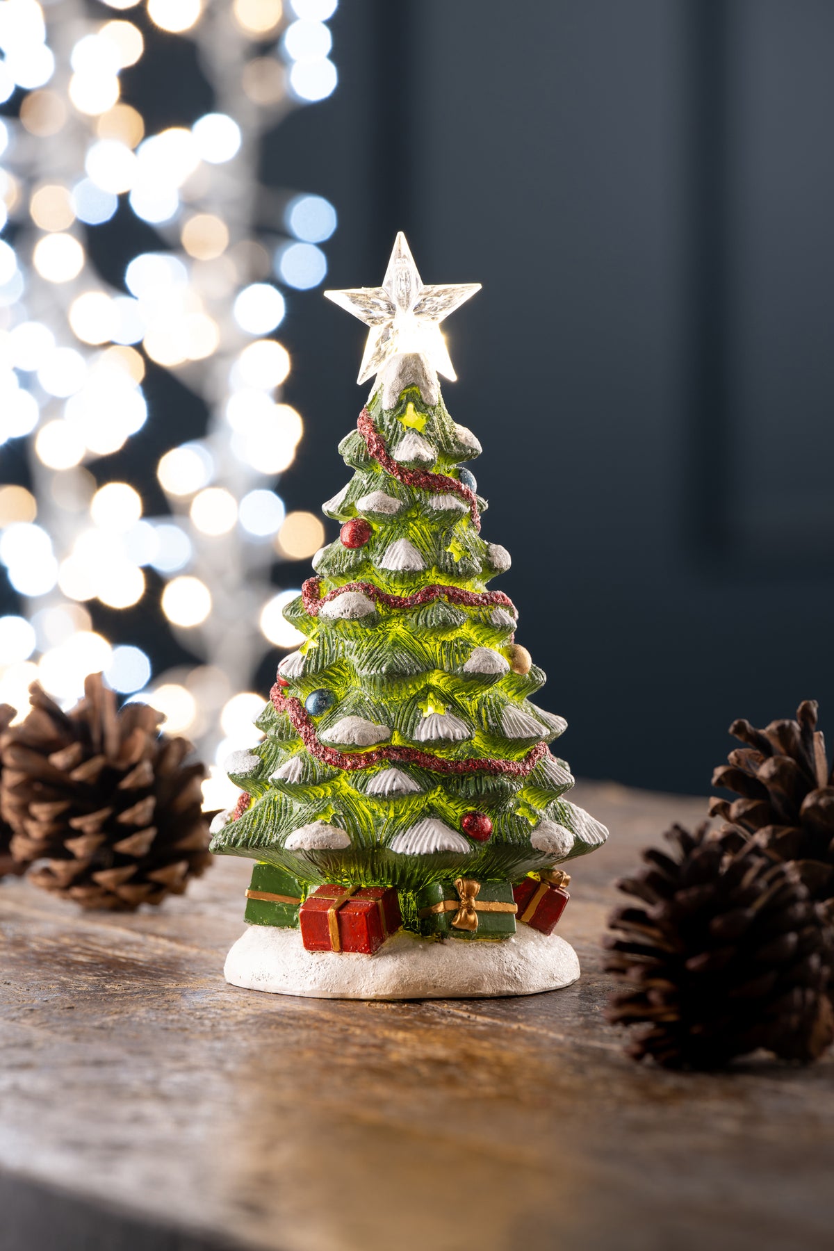 Aynsley Christmas Tree LED figurine with glowing star topper, red garland, and presents at the base on wood surface.