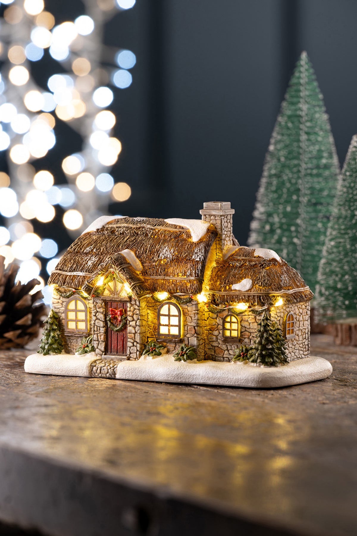 Aynsley Stone Thatched Cottage LED figurine with snow-dusted roof, lit windows, and Christmas wreath on door.