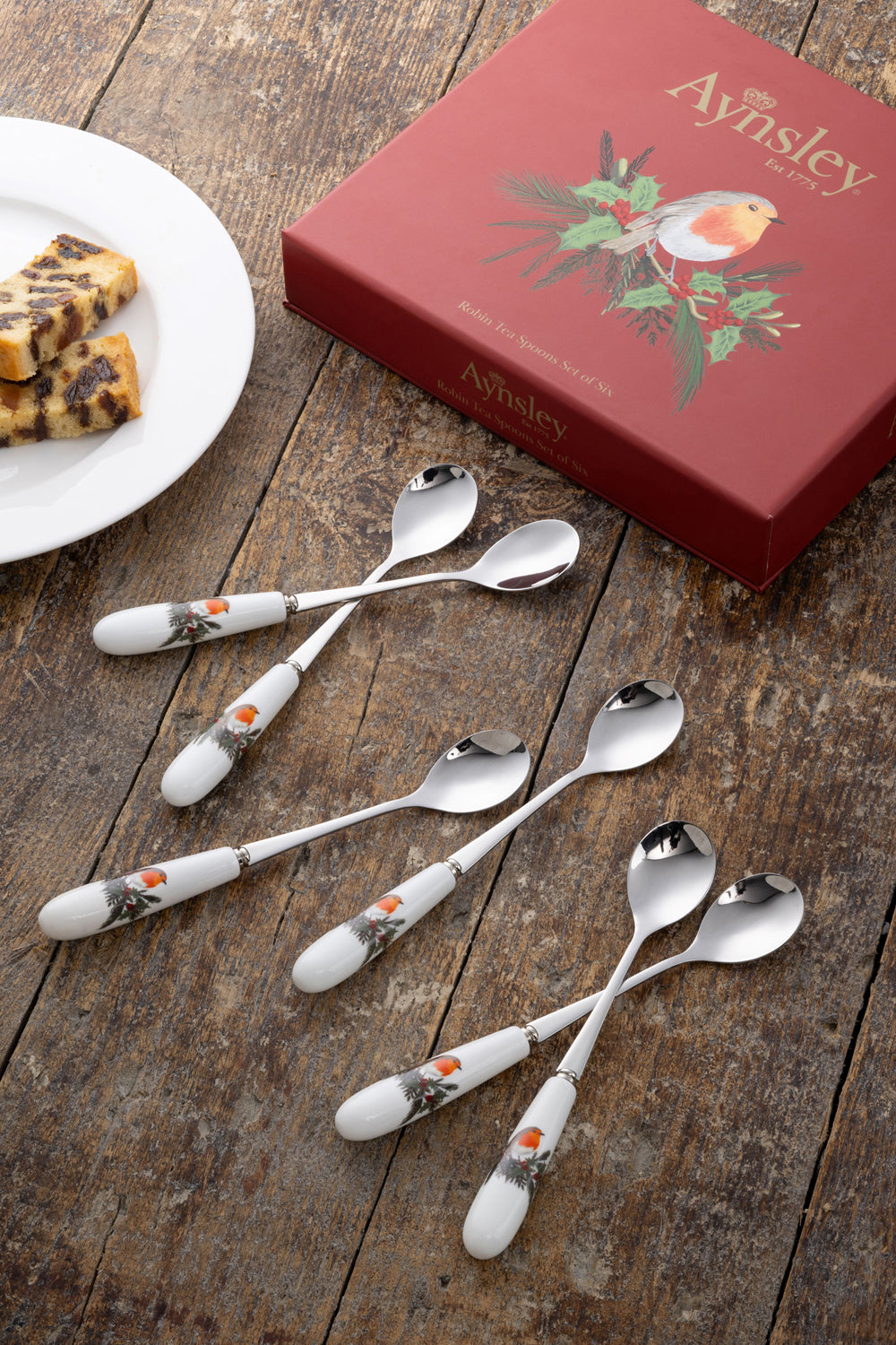 Set of six Aynsley Robin teaspoons with white handles featuring robin and holly design, next to red box and plate.