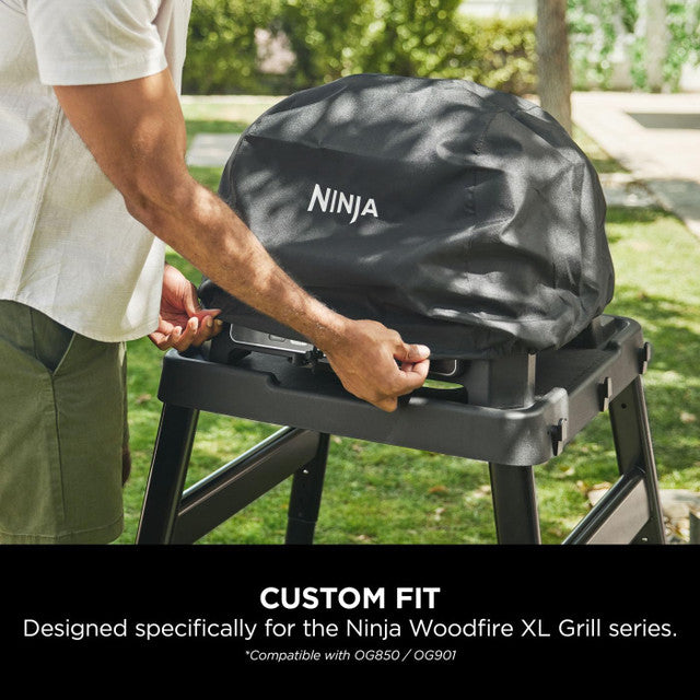 Black Ninja Woodfire XL Grill Cover fitted over a grill outdoors with hands adjusting the cover.