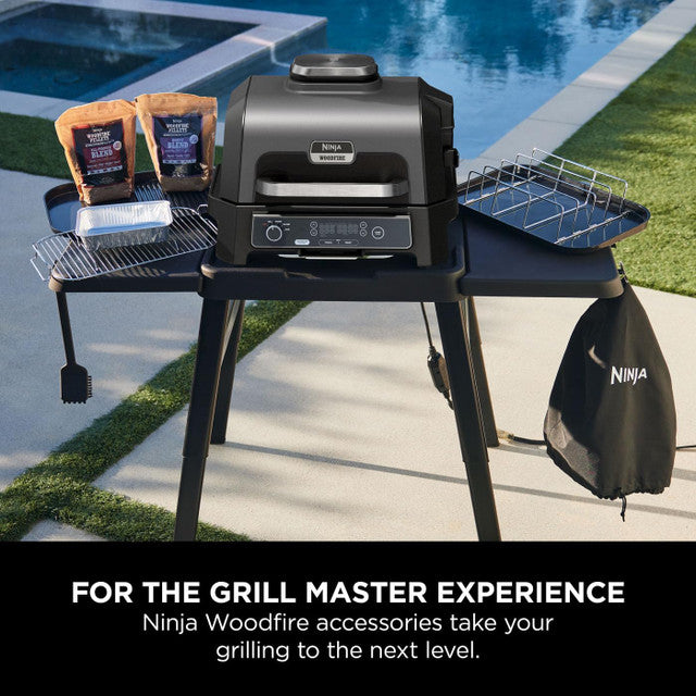 Black Ninja Woodfire XL Grill cover hanging on the side of a grill setup outdoors near a pool.