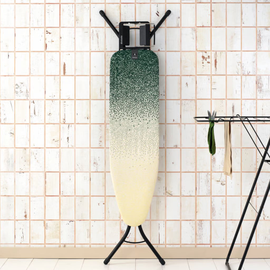 Brabantia Ironing Board A 110x30cm with green to cream gradient cover, standing upright against tiled wall.