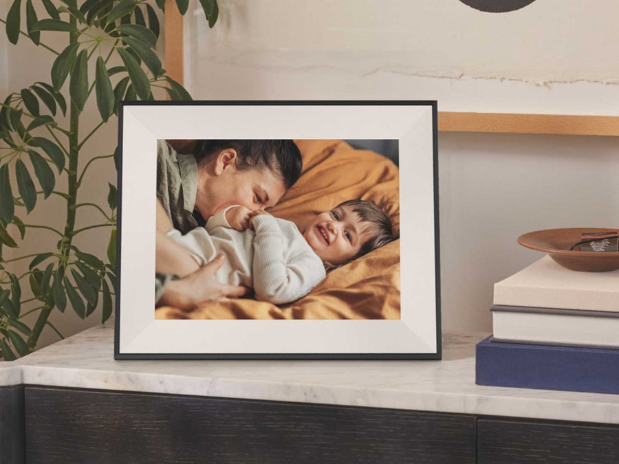 Aura Aspen 12'' digital photo frame in ink color displaying a photo of a smiling child and adult on a bed.