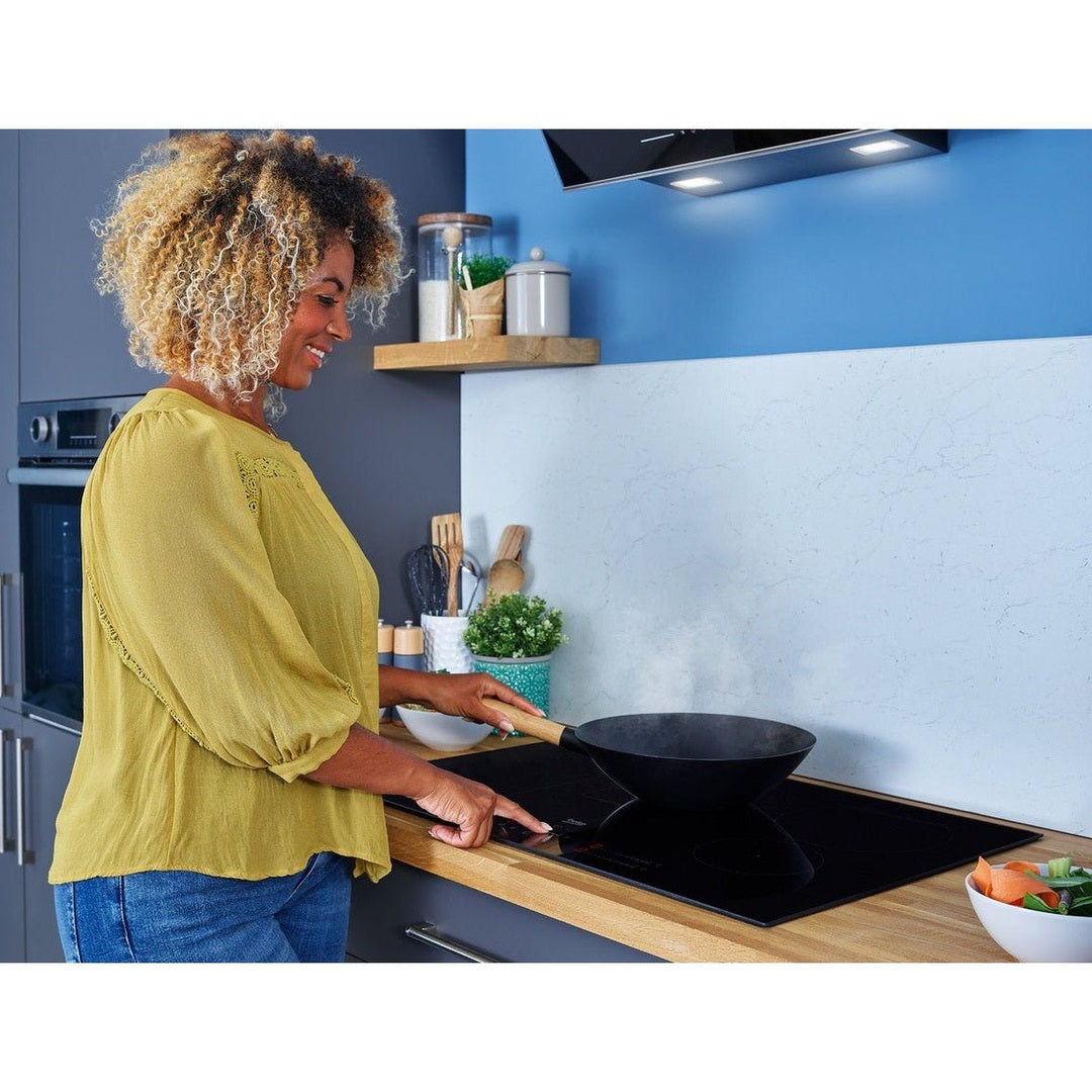Woman cooking on Beko 80cm induction hob with black wok and wooden countertop in modern kitchen.