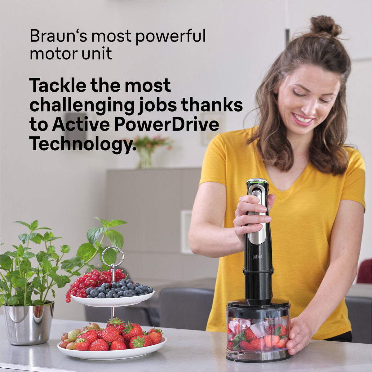 Woman using Braun Multiquick 9 Hand Blender black model MQ9138XI to blend fruit in a container on a kitchen counter.