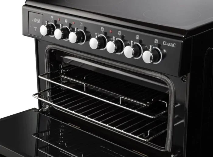 Rangemaster Classic 60cm black ceramic cooker with chrome knobs and open oven door showing two wire racks.