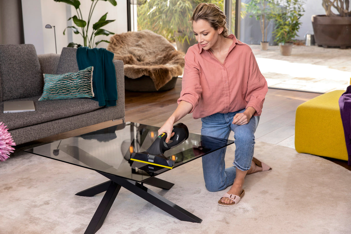 Woman using a Karcher WV5 Anniversary Window Vac to clean a glass coffee table in a living room.